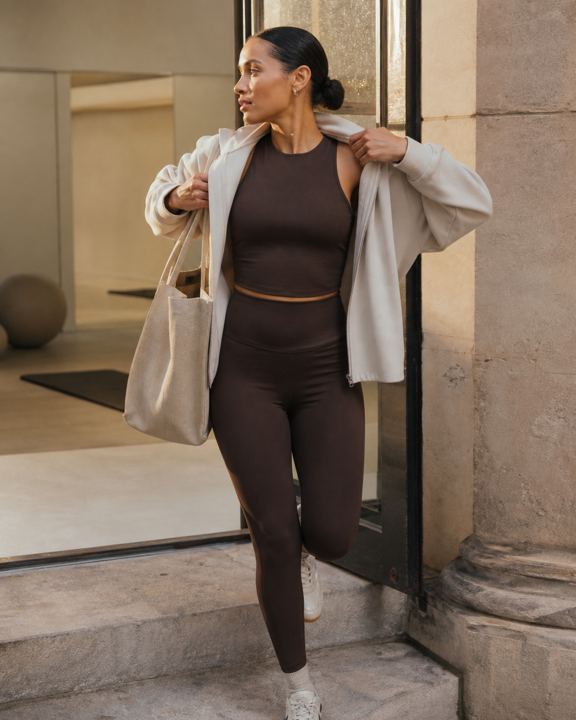 Woman moving from studio to street in cocoa activewear and an oat jacket