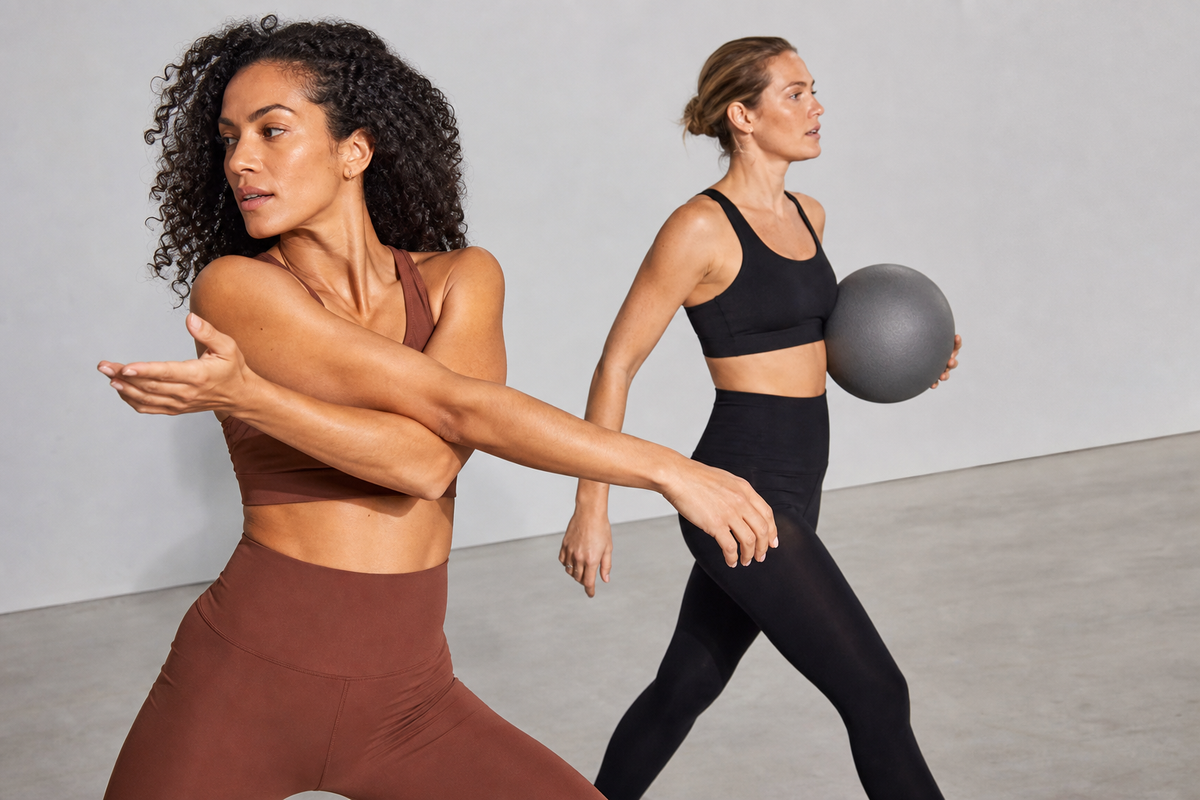 Two women in clay and black activewear moving through a studio