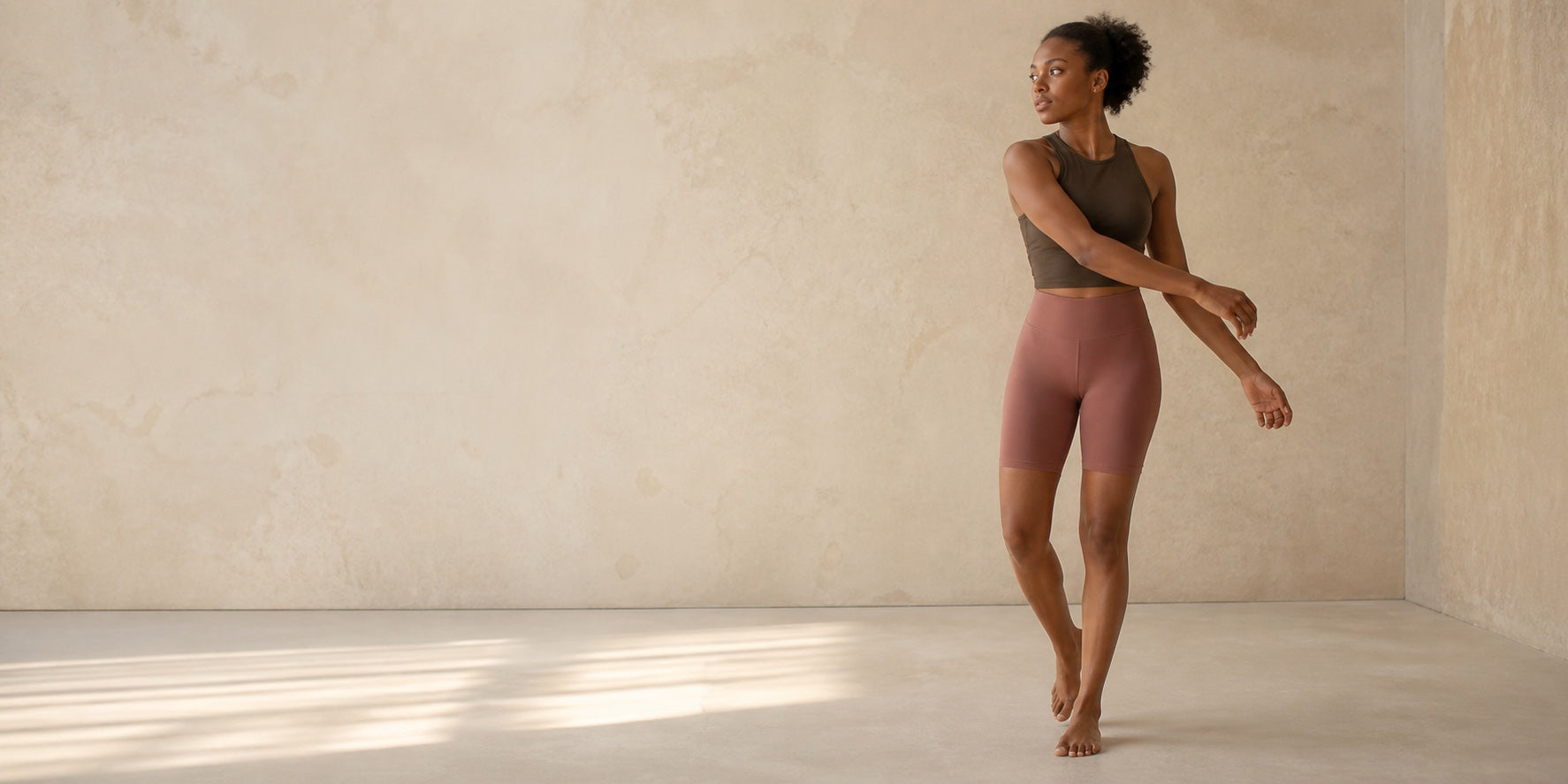Woman wearing a crop top and short leggings in a warm studio.
